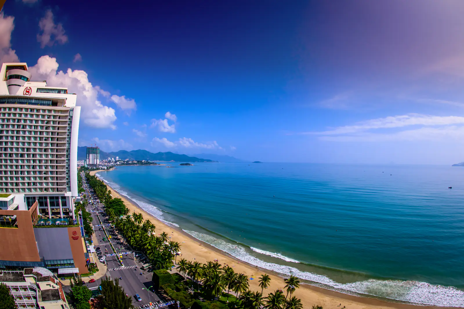 Bãi biển Trần Phú Nha Trang nhìn từ trên cao: dải cát vàng, hàng dừa và đường Trần Phú chạy dọc vịnh xanh, bên trái là khách sạn Sheraton