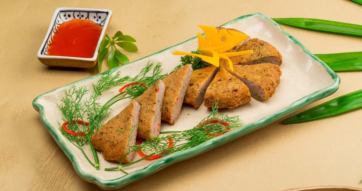 A plate of fried fish cake cut into triangles, garnished with dill and chili, next to a dish of chili sauce