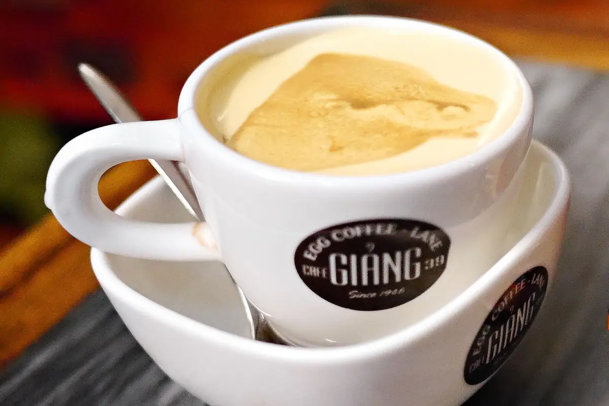 Tách cà phê trứng phủ lớp kem trứng vàng ngà có vệt cà phê, tách và đĩa in logo quán Giảng, thìa đặt trên đĩa, Hà Nội, tháng 7/2017