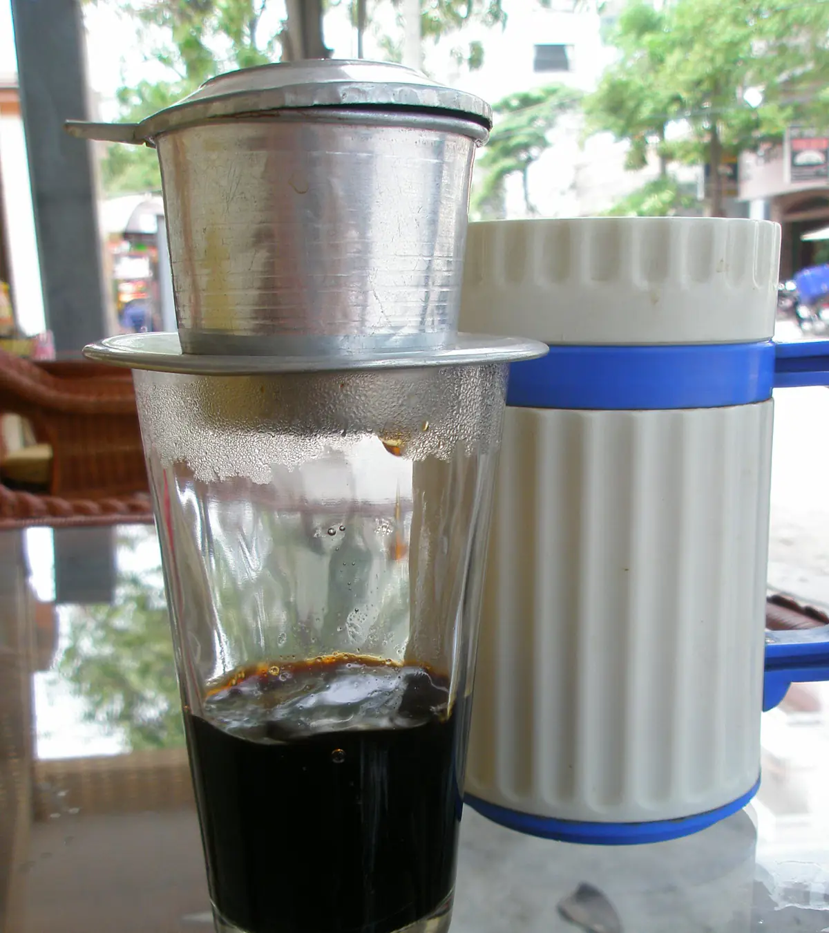 Phin nhôm đặt trên ly thủy tinh, cà phê đen nóng nhỏ giọt xuống đáy ly, bên cạnh là bình giữ nhiệt ở một quán cà phê Nha Trang, tháng 10/2007