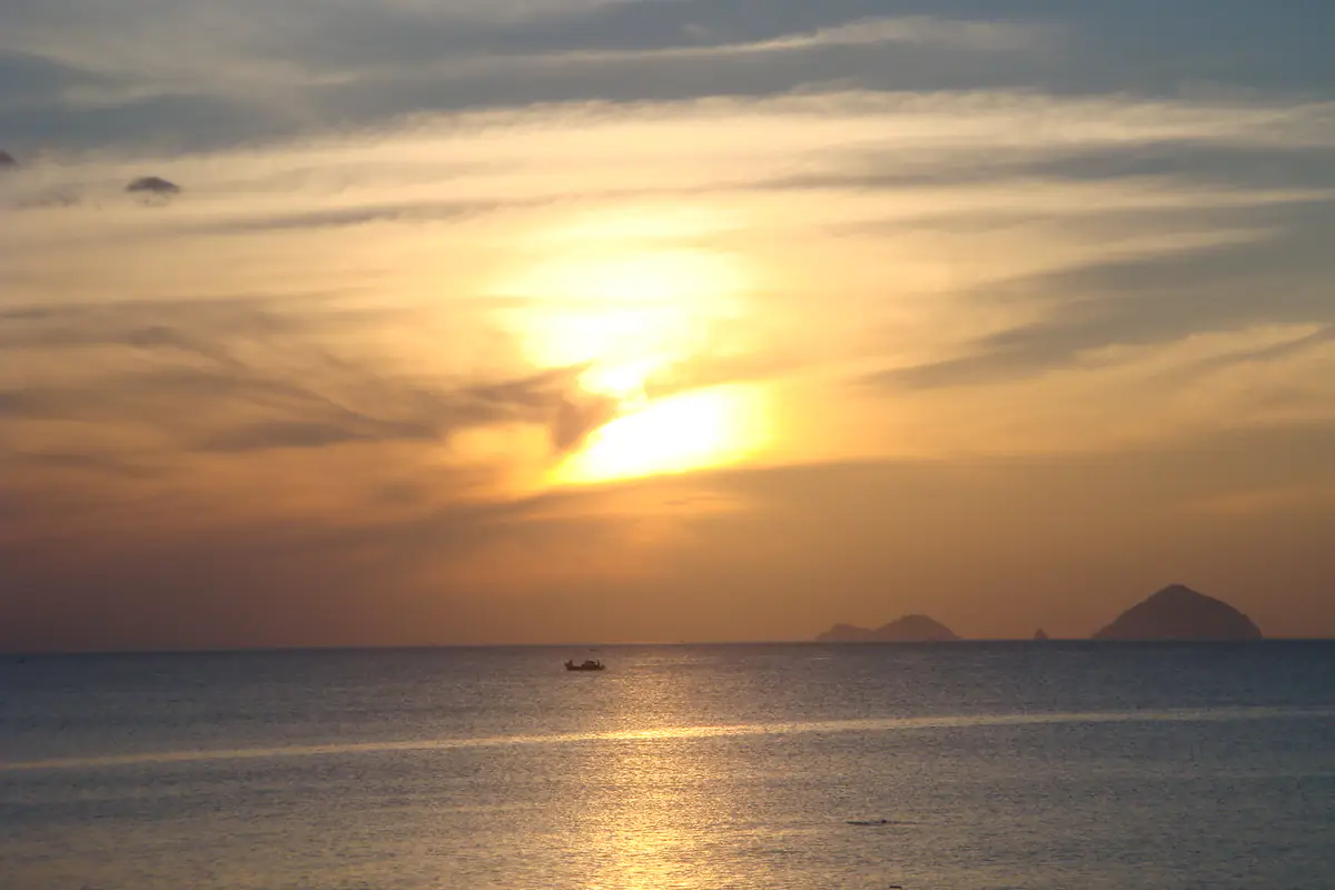 Mặt trời vừa lên sau lớp mây mỏng trên biển Nha Trang, một chiếc thuyền nhỏ và vài hòn đảo in bóng đen trên mặt nước ánh vàng, sáng tháng 8/2008