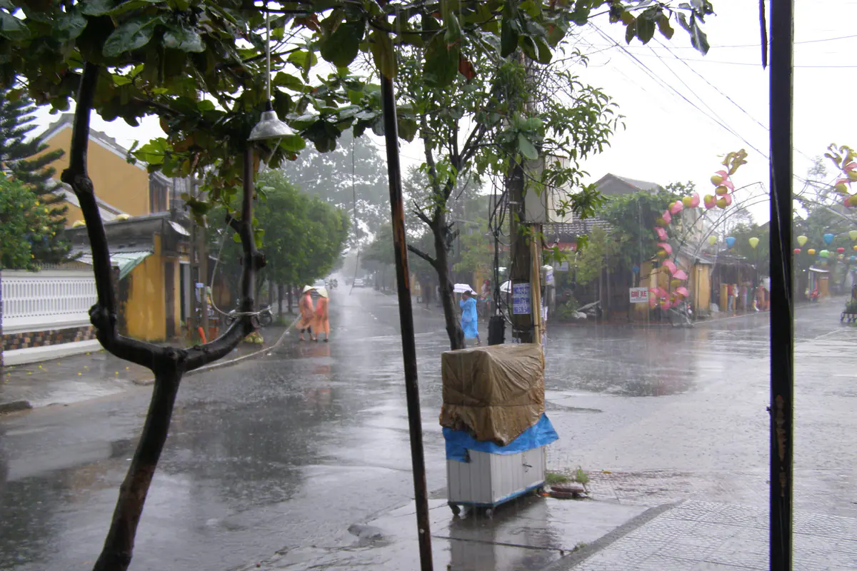 Một ngã tư ở Hội An trong cơn mưa lớn trưa 15/11/2013, mặt đường loang nước, vài người mặc áo mưa đội nón lá đi bộ, đèn lồng treo ven phố