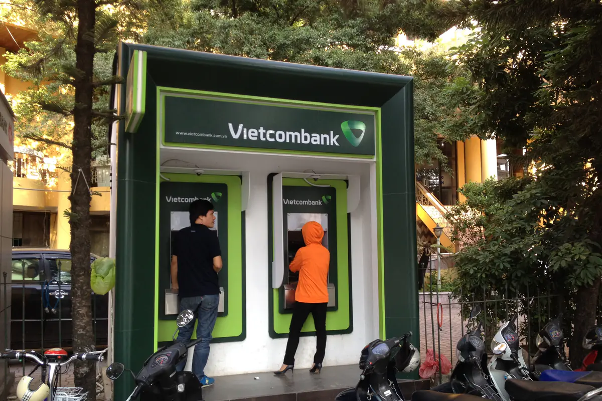 Hai người đang rút tiền tại buồng ATM đôi của Vietcombank bên hè phố Văn Cao - Đội Cấn, Hà Nội, xe máy đỗ dọc hàng rào bên cạnh, tháng 10/2015