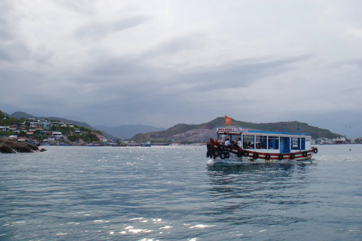 Tàu du lịch chạy trên vịnh Nha Trang gần khu Cầu Đá ngày trời nhiều mây, phía sau là đồi và dãy núi, tháng 8/2010