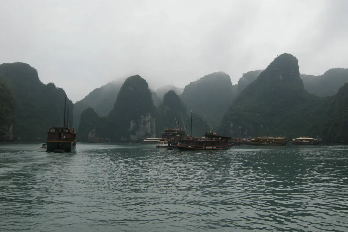 Sương mù che đỉnh các đảo đá trên vịnh Hạ Long buổi sáng, vài tàu gỗ neo trên mặt nước xám, tháng 3/2008