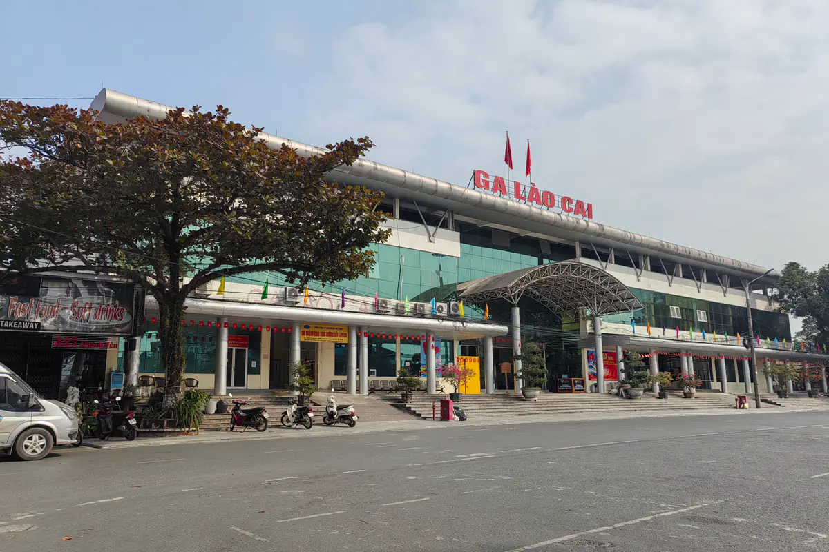 Mặt tiền ga Lào Cai với dòng chữ Ga Lào Cai trên mái, bậc thềm rộng và quảng trường trước ga, tháng 12/2025