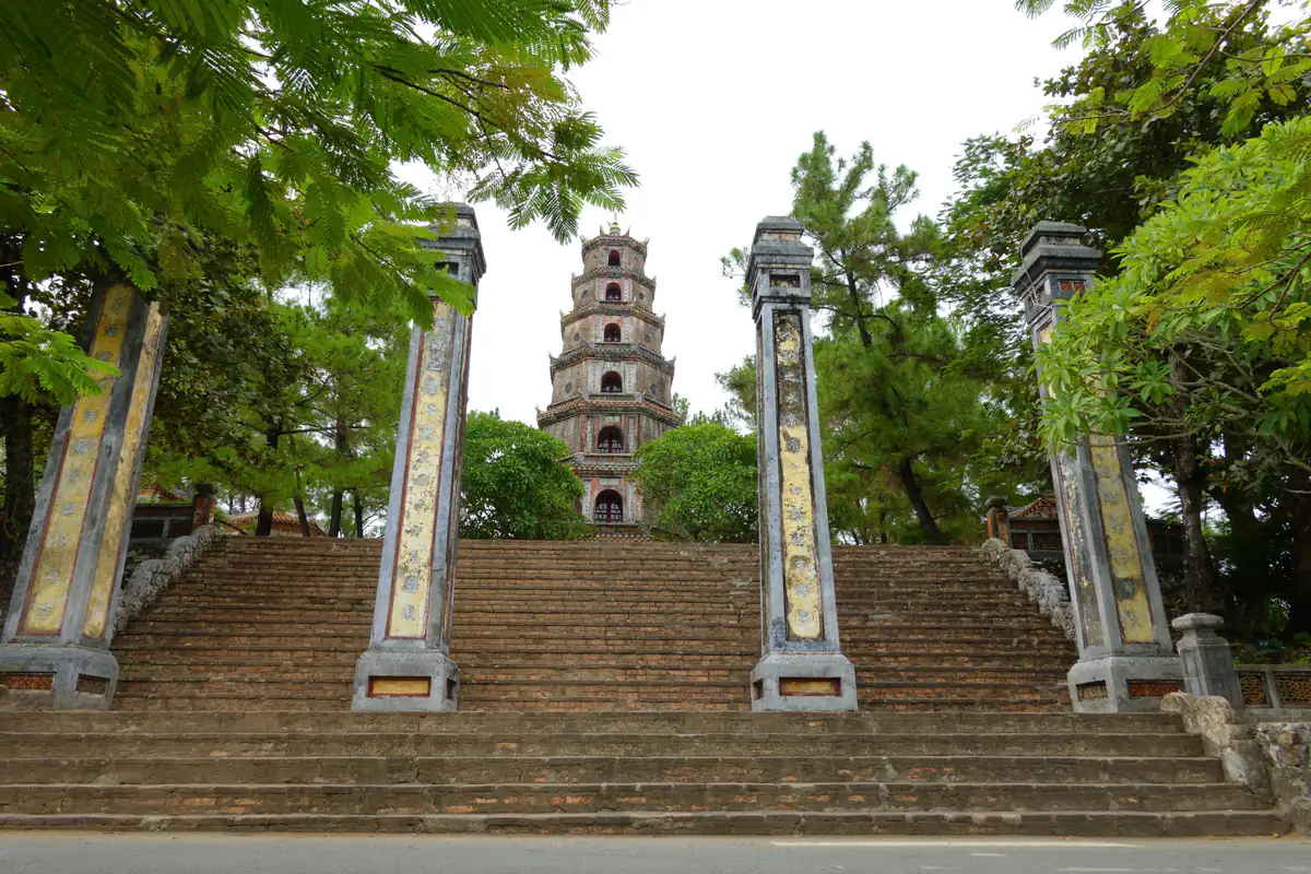 Bậc đá dẫn lên cổng chùa Thiên Mụ ở Huế, bốn trụ biểu hai bên, phía sau là tháp Phước Duyên bảy tầng giữa tán cây, tháng 9/2024