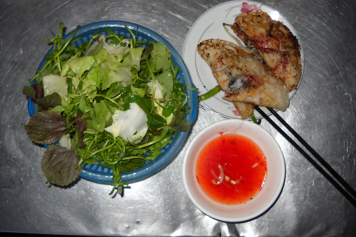 Hai chiếc bánh xèo nhân mực cỡ nhỏ ở Nha Trang trên đĩa trắng, bên cạnh rổ rau sống gồm xà lách, tía tô, rau thơm và chén nước chấm màu đỏ, ảnh tải lên tháng 6/2012