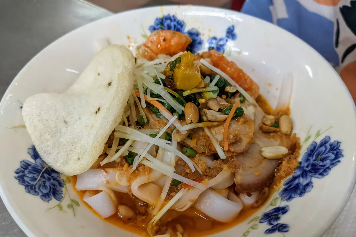 Tô mì Quảng tôm thịt ở Đà Nẵng: sợi mì gạo to bản, tôm, thịt heo, đậu phộng rang, giá, hành lá, chút nước dùng màu nghệ và miếng bánh tráng gác trên miệng tô, tháng 6/2022
