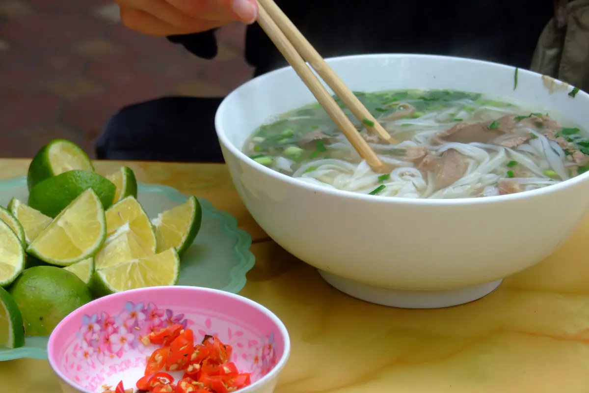 Tô phở bò nóng ở quận Cầu Giấy, Hà Nội: bánh phở, thịt bò thái mỏng, hành lá trong nước dùng trong, bên cạnh đĩa chanh cắt múi và chén ớt tươi, tháng 4/2012