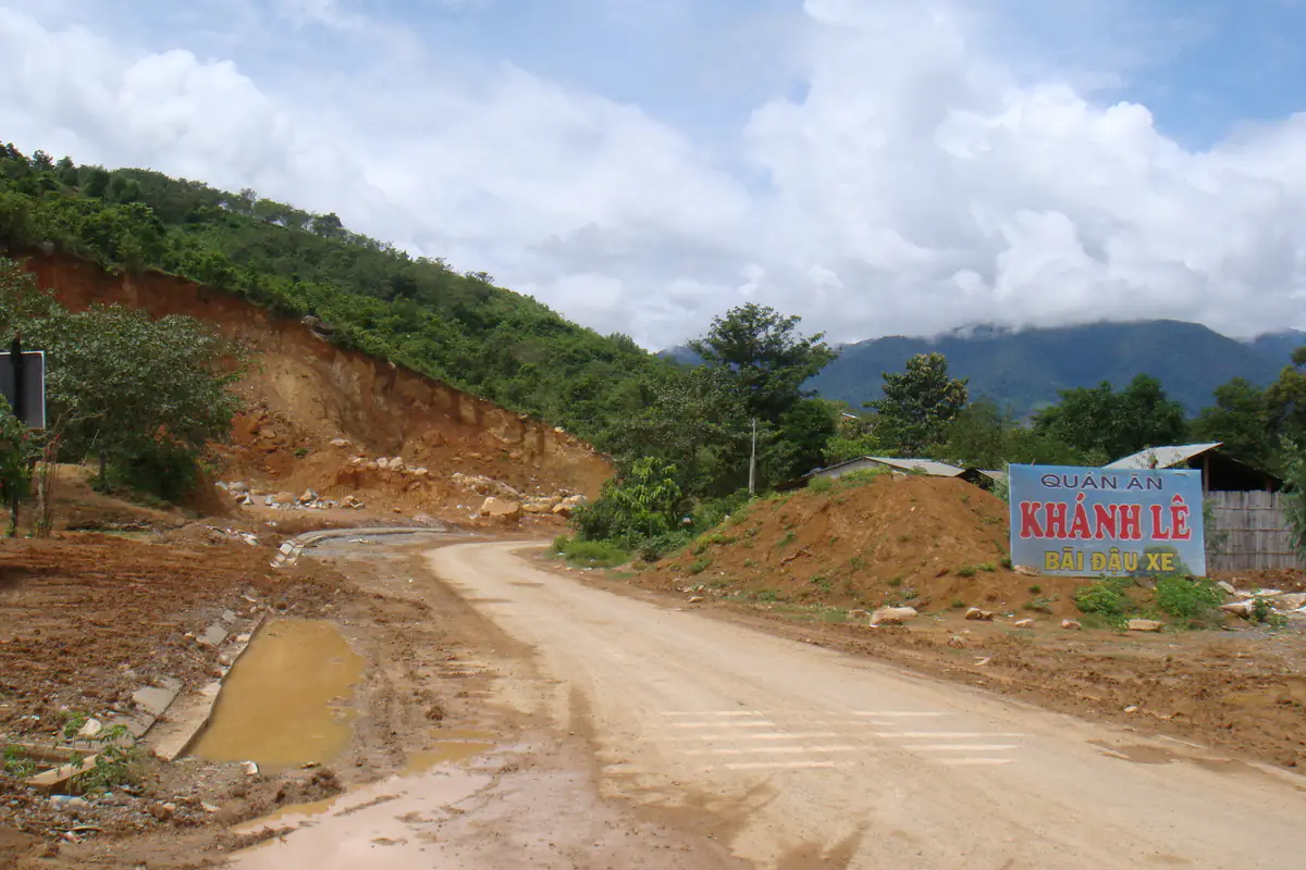 Quán ăn và bãi đậu xe mang tên Khánh Lê bên con đường đất đang làm trên chặng Đà Lạt - Nha Trang, vách taluy đất đỏ bên trái, núi mây phía xa, tháng 8/2010