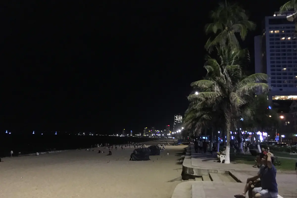 Lối đi dạo ven bãi biển Trần Phú Nha Trang buổi tối, hàng dừa và khách sạn cao tầng lên đèn, người ngồi hóng gió trên ghế đá