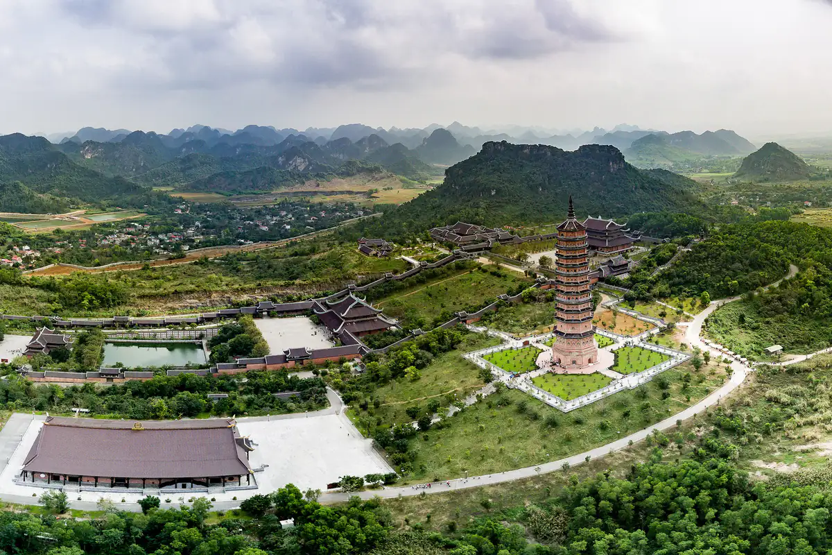 Toàn cảnh chùa Bái Đính, Ninh Bình nhìn từ trên cao với bảo tháp nhiều tầng, các mái điện và đường đi giữa đồi cây, phía xa là dãy núi đá vôi, tháng 8/2017