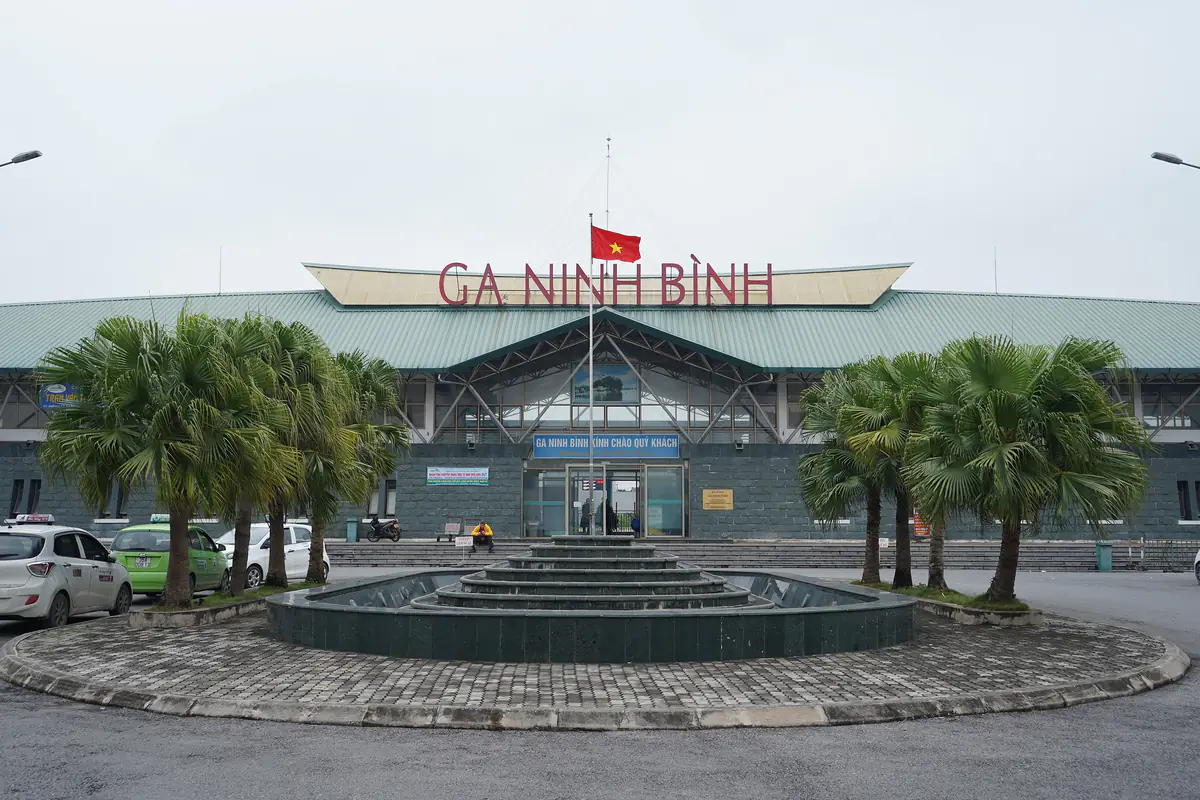 Mặt tiền ga Ninh Bình với dòng chữ Ga Ninh Bình trên mái, hàng cọ và đài phun nước ở quảng trường trước ga, tháng 1/2020