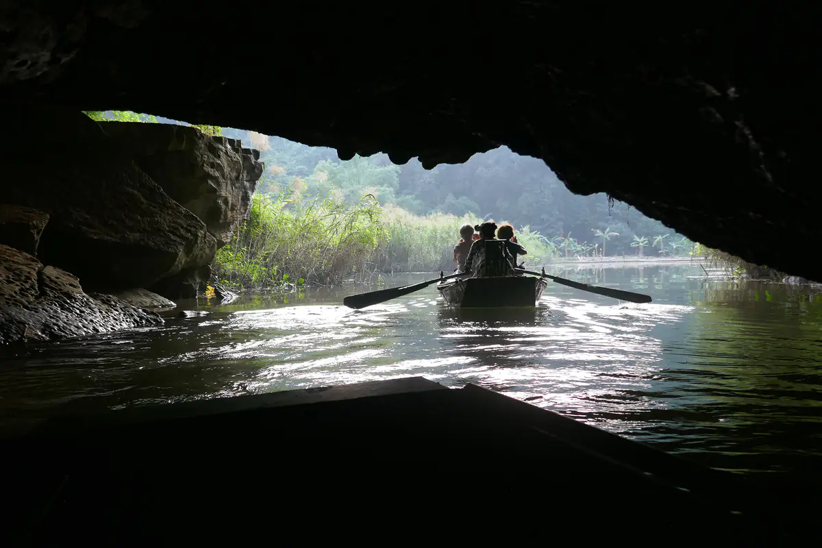 Nhìn từ trong lòng hang tối ra cửa hang sáng ở Tam Cốc, một chiếc đò chở khách đang chèo qua, hai bên là vách đá và lau sậy, tháng 11/2017