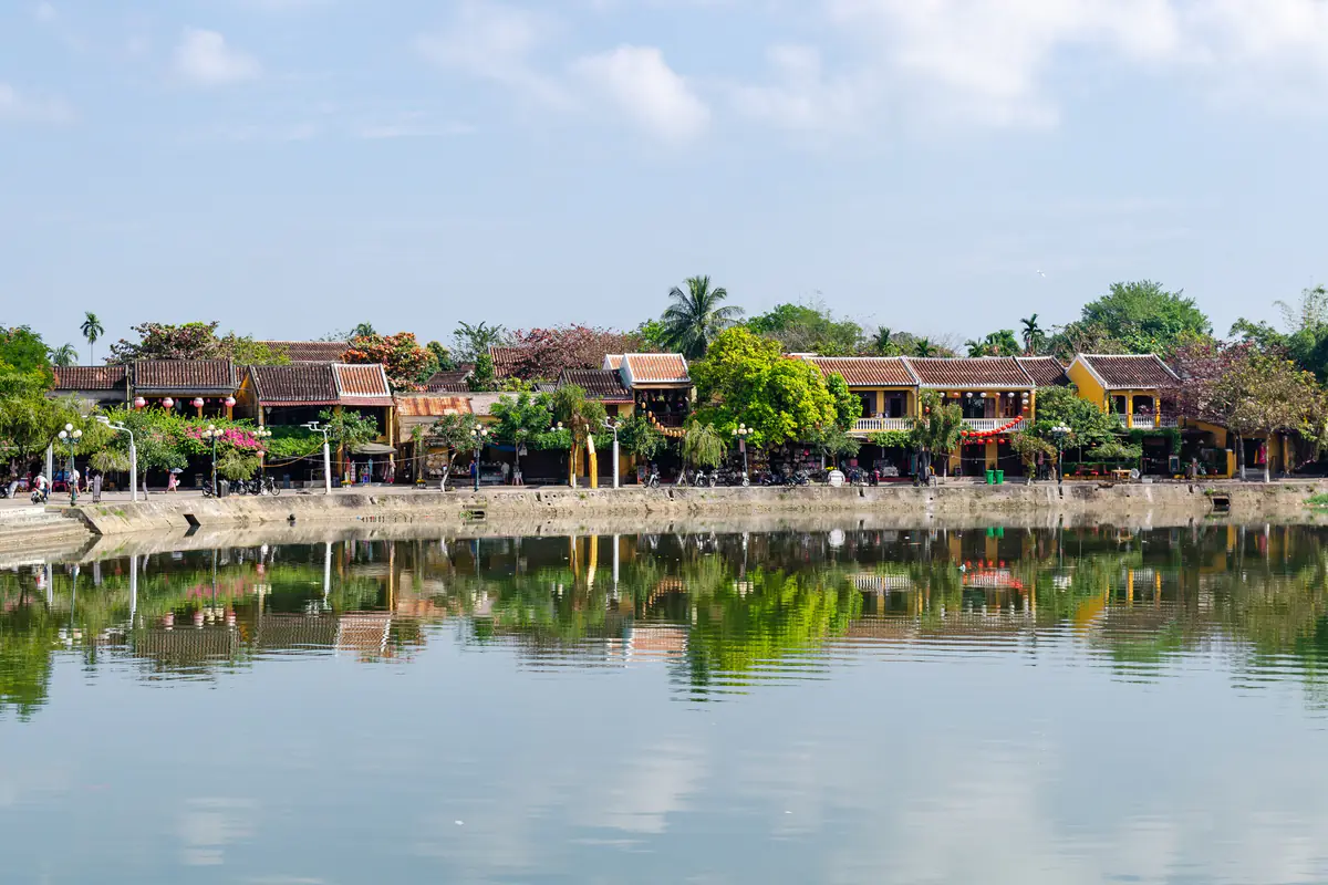 Dãy nhà tường vàng mái ngói ven sông ở phía tây nam phố cổ Hội An, bóng nhà và cây soi xuống mặt nước phẳng lặng, nhìn từ cầu Hồng Lãnh, tháng 1/2020