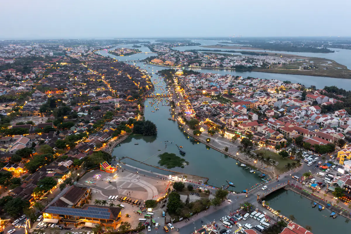 Phố cổ Hội An nhìn từ trên cao lúc chạng vạng, sông Hoài chảy giữa hai bờ nhà mái ngói đã lên đèn, phía xa là các nhánh sông Thu Bồn, tháng 4/2024