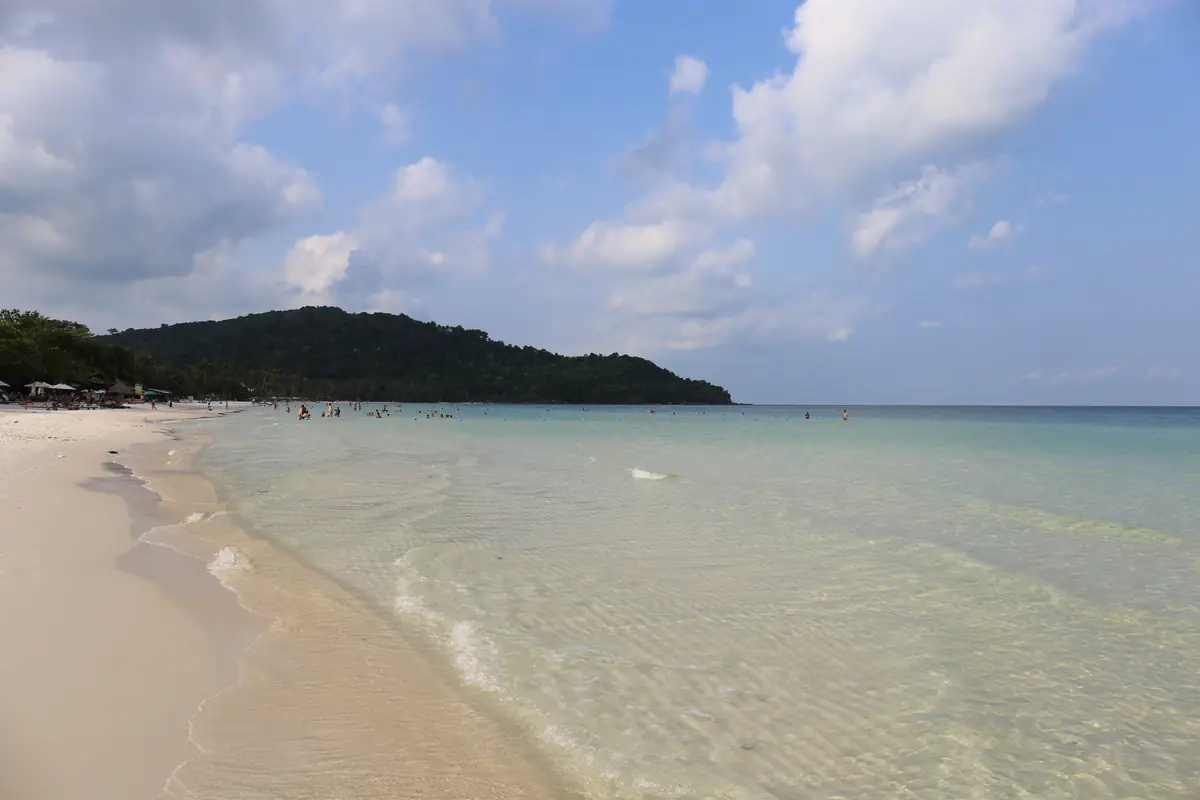 Bãi Sao ở phía nam đảo Phú Quốc, cát trắng, nước nông trong xanh, vài người tắm phía xa dưới chân đồi cây, trời nắng nhiều mây, tháng 3/2016