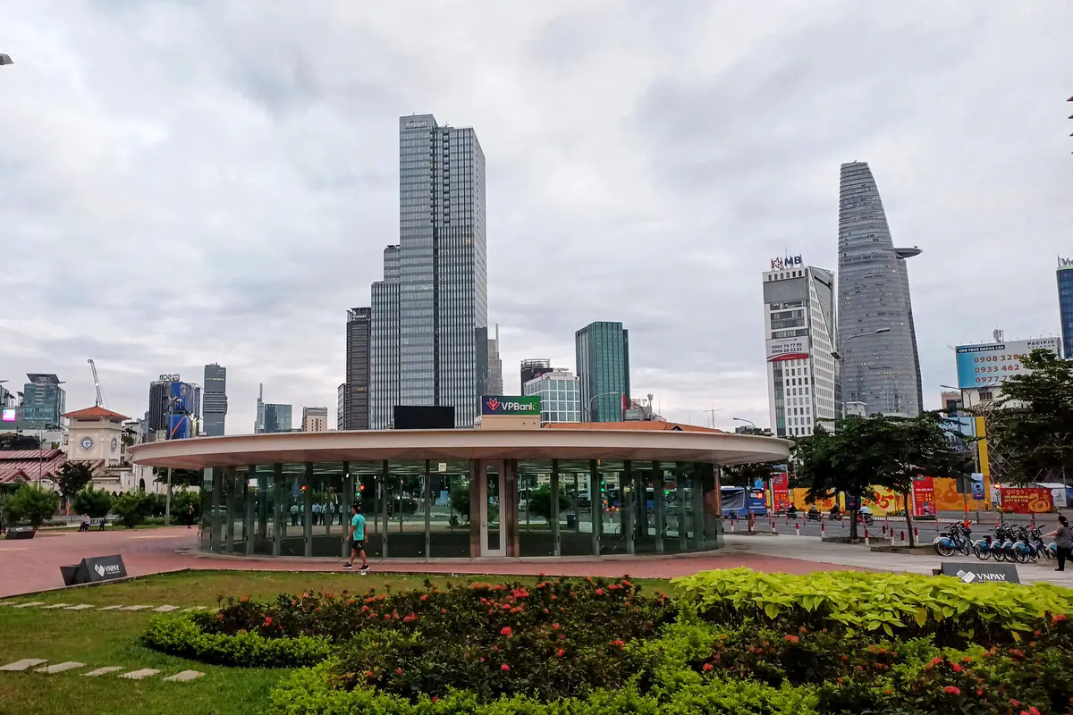 Giếng trời tròn bằng kính của ga ngầm Bến Thành, metro số 1, trên quảng trường trước chợ Bến Thành, phía sau là các tòa nhà cao tầng trung tâm, sáng 25/12/2024