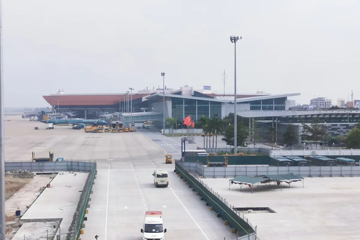Nhà ga nội địa T1 sân bay Nội Bài mái đỏ nhìn từ nhà ga quốc tế T2, phía trước là đường nội bộ trên sân đỗ có xe phục vụ chạy qua, tháng 12/2023