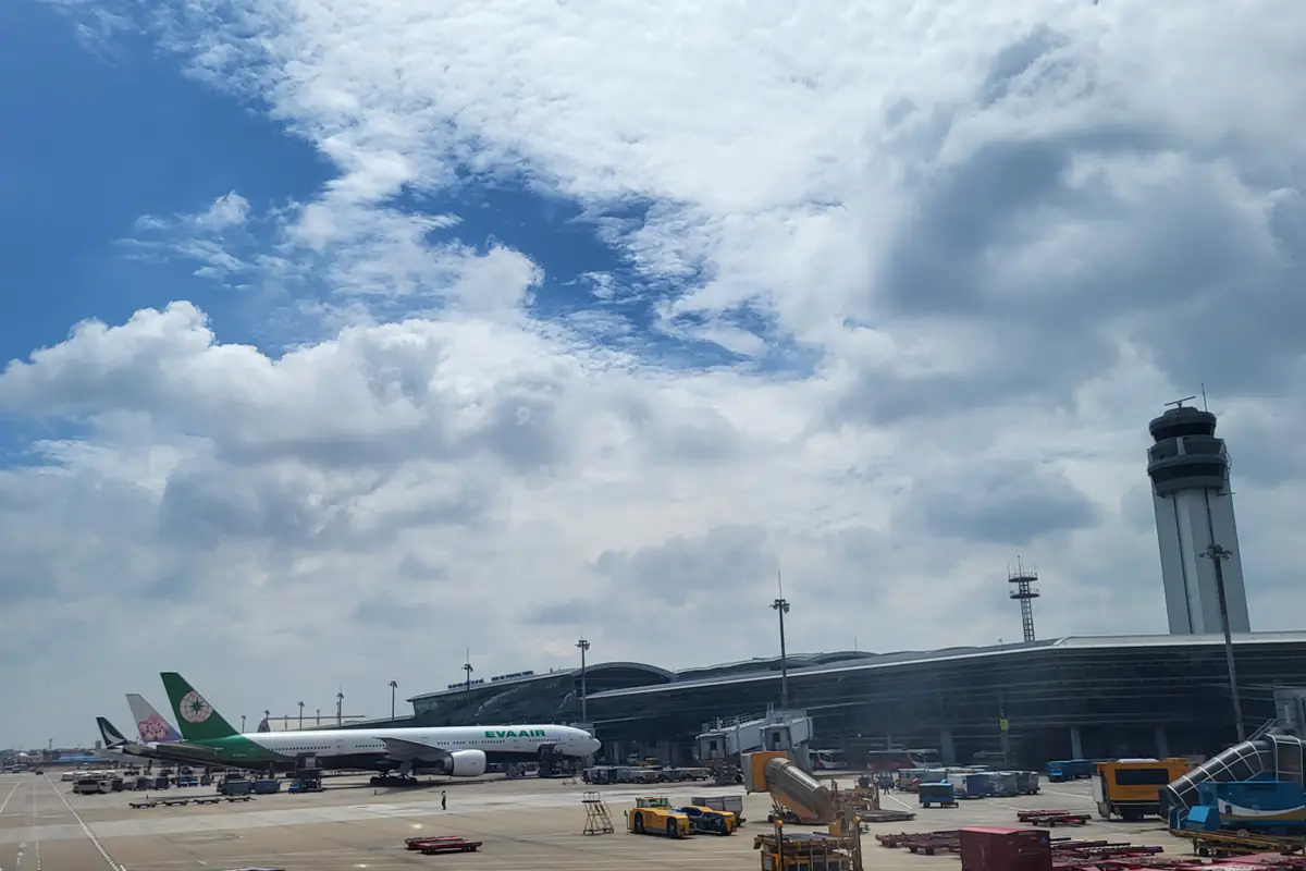 Nhà ga quốc tế T2 sân bay Tân Sơn Nhất mái vòm cong và đài kiểm soát không lưu dưới trời nhiều mây, phía trước là máy bay đỗ ở ống lồng và xe phục vụ mặt đất, tháng 8/2026