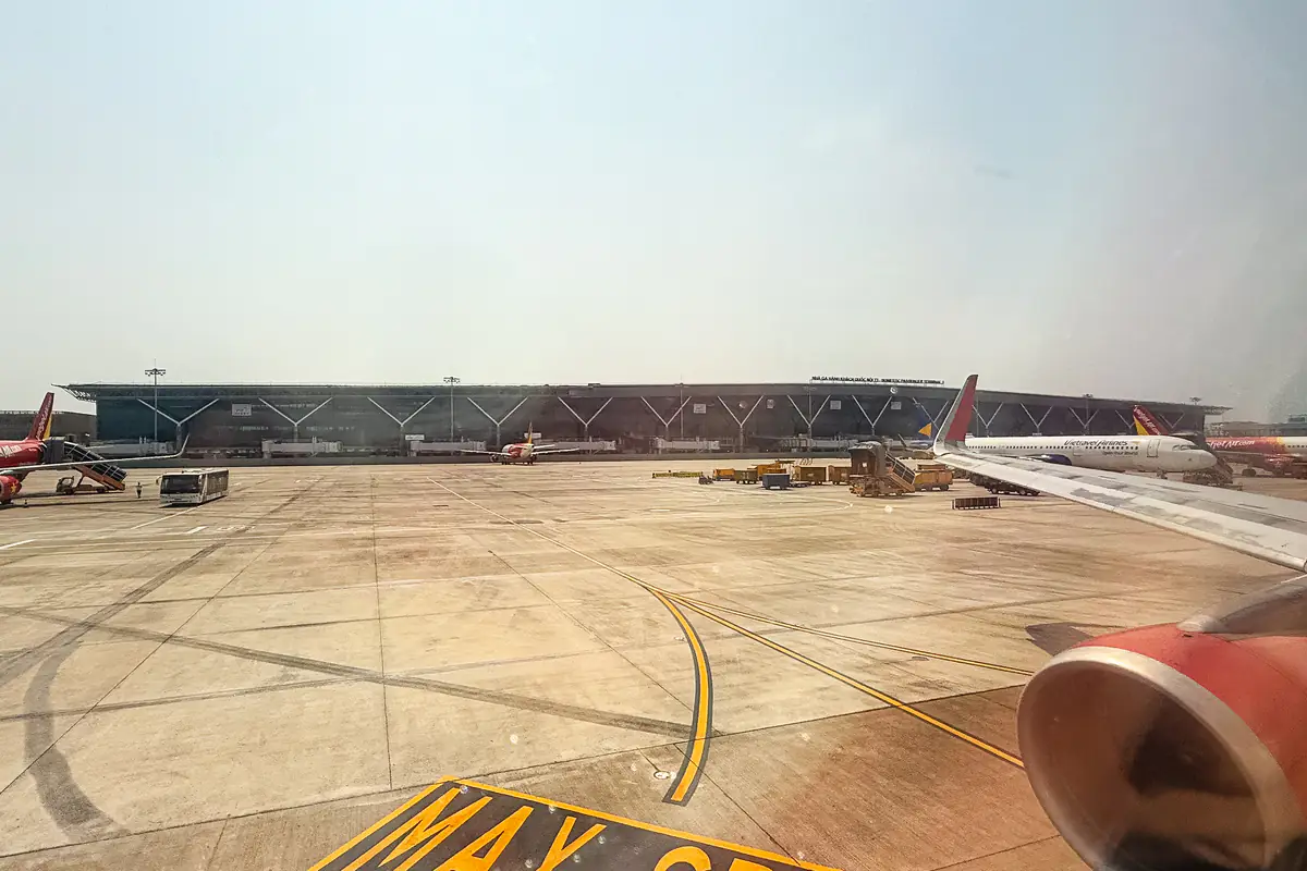 Nhà ga T3 sân bay Tân Sơn Nhất mái thấp kéo dài nhìn qua cửa sổ máy bay trên sân đỗ, phía trước là vạch kẻ đường lăn và vài máy bay đỗ, tháng 1/2025