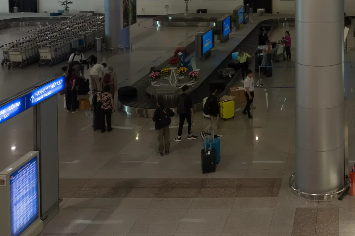 Hành khách kéo vali quanh băng chuyền hành lý ở sảnh đến quốc tế sân bay Tân Sơn Nhất, TP.HCM, bên trái là biển chỉ lối ra và quầy hành lý thất lạc, tháng 8/2023