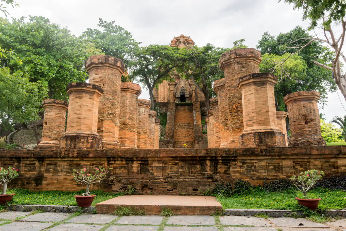 Hai hàng cột gạch tiền đình ở Tháp Bà Ponagar, phía sau là đỉnh tháp chính giữa tán cây