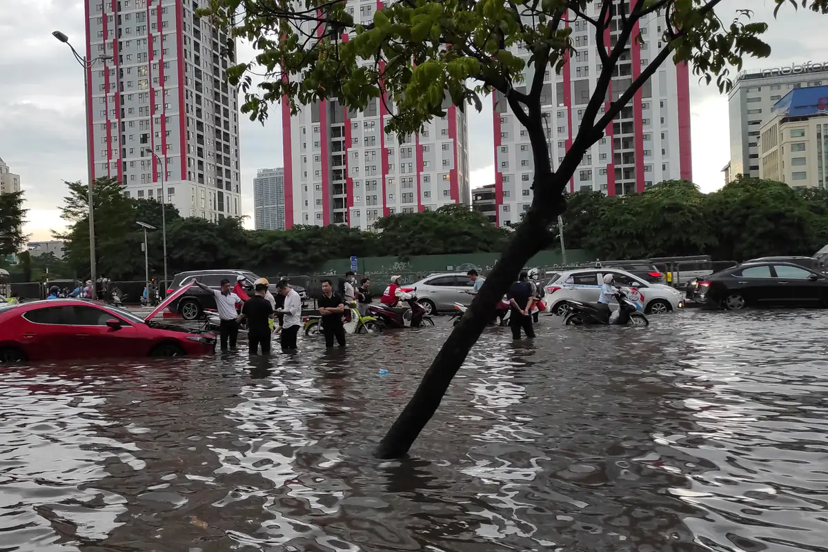 Đường Phạm Hùng gần cầu vượt Mai Dịch ngập sau mưa lớn, một ô tô đỏ chết máy giữa nước, người dắt xe máy lội qua, chiều 29/5/2022