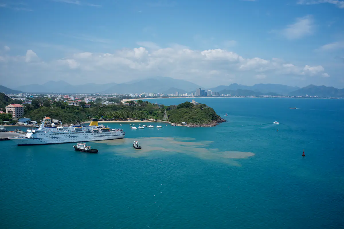 Vịnh Nha Trang nhìn từ trên cao về phía đất liền: mặt nước xanh lặng, một tàu du lịch biển neo ở cảng, vài tàu nhỏ trong vịnh, phố và núi phía sau, cuối tháng 2/2012