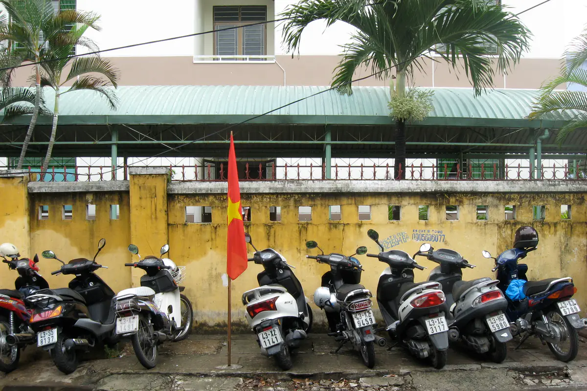 Dãy xe số và xe tay ga đỗ sát bức tường vàng trên vỉa hè ở Đà Nẵng, một lá cờ cắm giữa hàng xe, tháng 4/2009