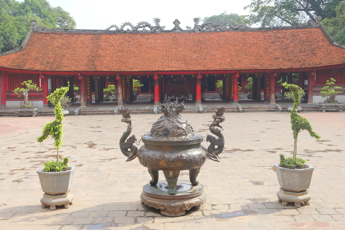 Lư hương đồng có quai rồng giữa sân lát gạch khu Đại Thành, hai chậu cây cắt dáng chim hạc, phía sau là nhà Bái đường mái ngói đỏ, cột sơn son, Văn Miếu - Quốc Tử Giám, tháng 8/2014