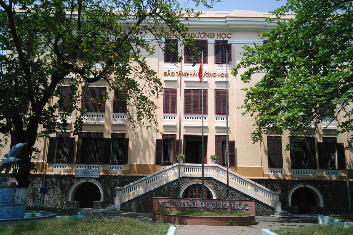 Mặt tiền tòa nhà chính của Viện Hải dương học ở Cầu Đá, Nha Trang, có bảng tên Bảo tàng Hải dương học, cầu thang đôi dẫn lên cửa chính và hàng cây hai bên, tháng 3/2016